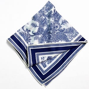 May include: A folded square handkerchief with a blue and white paisley pattern. The border features alternating stripes of white and navy blue, with a white trim. The handkerchief is made of a soft, possibly silk, material.