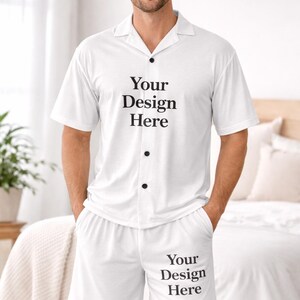 May include: White pyjama set with short sleeves and shorts. The shirt has a collar and black buttons. The text "Your Design Here" is printed on the shirt and shorts. The model is wearing the set.