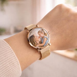 May include: A rose gold wristwatch with a mesh band. The watch face displays a color photograph of a mother and child. The watch is secured on a wrist.
