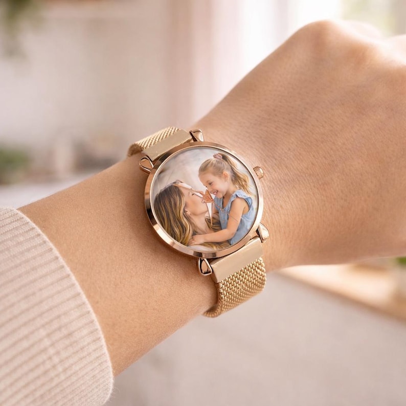 May include: A rose gold wristwatch with a mesh band. The watch face displays a color photograph of a mother and child. The watch is secured on a wrist.