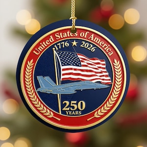Pode incluir: Um ornamento redondo azul, vermelho e dourado com o texto "United States of America 1776-2026" e "250 YEARS". O ornamento apresenta uma bandeira americana e um jato azul.