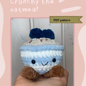 Könnte beinhalten: Gehäkeltes Haferflocken-Plüschtier mit einem lächelnden Gesicht, blau-weißen Streifen und braunen Füßen. Das Plüschtier hat ein dunkelblaues Topping und den Text "Crunchy the oatmeal" und "PDF pattern".
