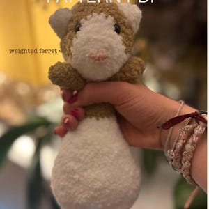 Könnte beinhalten: Ein handgefertigtes, gewichtetes Frettchen-Plüschtier mit weißem Körper und braun-weißem Kopf. Der Text "PATTERN PDF" steht oben und "weighted ferret" links. Das Frettchen wird in einer Hand gehalten.
