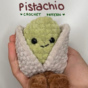 Peut inclure: Un jouet en peluche crocheté en forme de pistache avec un centre texturé vert clair, une enveloppe beige et des détails marron à la base. Le texte au-dessus indique Pistachio CROCHET PATTERN. La peluche a deux petits yeux noirs et un sourire.