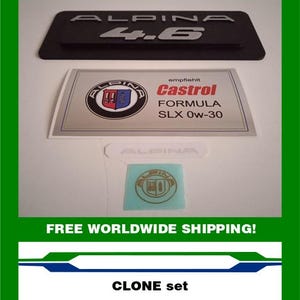 May include: A set of Alpina car emblems and stickers. The set includes a black emblem with "ALPIN 4.6" in silver, a Castrol oil sticker, and a small Alpina sticker. The text "CLONE set" is also visible.
