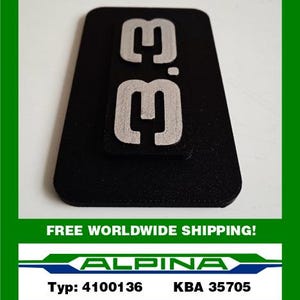 May include: A black rectangular emblem with the silver text "3.3" on a smaller, attached rectangle. The emblem is set against a white background with a green border. Below, the text "ALPINA" is displayed with the text "Typ: 4100136 KBA 35705".
