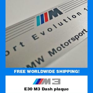 Könnte beinhalten: Silberne Armaturenbrettplakette mit dem BMW-Logo in Blau, Rot und Türkis. Der Text "Evolution 1" und "MW Motorsport" ist auf der Plakette aufgedruckt. Der Text "E30 M3 Dash plaque" ist ebenfalls sichtbar.