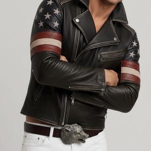May include: Black leather jacket with American flag design on the sleeves. The jacket features a classic biker style with a notched collar, zipper closure, and a silver wolf buckle belt. The sleeves have a star and stripe design.