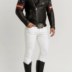 May include: Black leather jacket with American flag design on the sleeves, paired with white pants and black boots. The jacket has a zipper closure and a notched collar. A silver belt buckle adds a decorative touch.