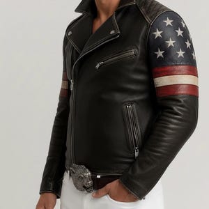 May include: Black leather jacket with an asymmetrical zipper, featuring an American flag design on the sleeves. The jacket has a quilted shoulder detail and a silver wolf buckle on the belt. The jacket is worn with white pants.
