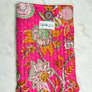 May include: A quilted, hot pink fabric case with a floral pattern in green, orange, and white. The case has a button closure and a label that reads "Pipette & Co."