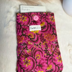 Peut inclure: Une housse de livre rose avec un motif floral jaune et marron. La housse est fermée par un bouton rose et porte une étiquette blanche avec le texte "Pipilette & Co." Le livre à l'intérieur est intitulé "Jacques Prévert Paroles".