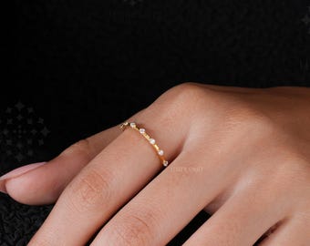 May include: A thin gold band ring featuring a series of small, clear, round-cut stones set along the top half of the band. The ring is worn on a finger, showcasing the delicate metalwork and the evenly spaced, sparkling stones embedded in the gold.