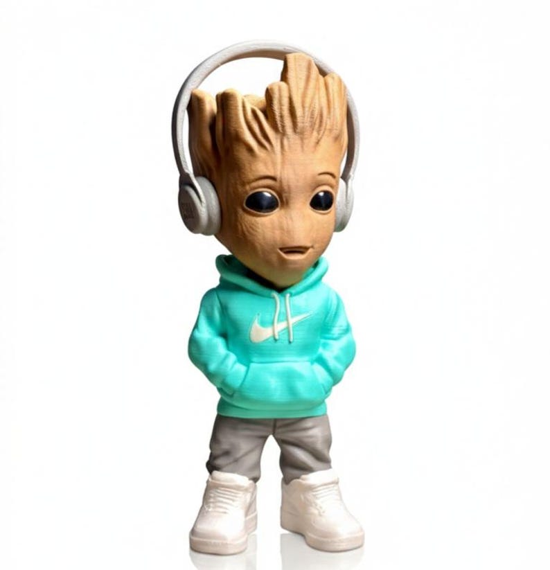 Op de afbeelding: Een Groot-beeldje met een turquoise hoodie met een wit Nike-logo, een grijze broek, witte sneakers en een grijze koptelefoon. Het beeldje heeft een houten textuur en zwarte ogen, tegen een witte achtergrond.