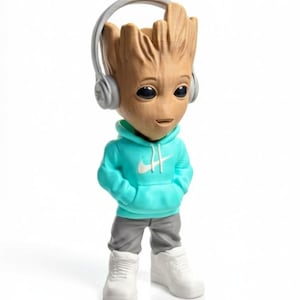 Op de afbeelding: Een beeldje van Groot met een turquoise hoodie met een wit Nike-logo, een grijze broek en witte sneakers. Het beeldje heeft een koptelefoon en een glimlachende uitdrukking. Een verzamelobject.