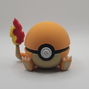 May include: A spherical orange and tan figurine resembling a ball with a central black and white circular button. The figure features two small tan feet with white claws and a tail extending from the back, topped with a red and yellow flame.