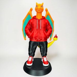 Könnte beinhalten: Eine 3D-gedruckte Charizard-Figur mit rotem Kapuzenpullover, schwarzer Hose und roten Turnschuhen. Die Figur hat orange Haut, blaue Augen und Flügel mit orangefarbenen und türkisfarbenen Akzenten. Sie steht auf einem schwarzen Sockel.