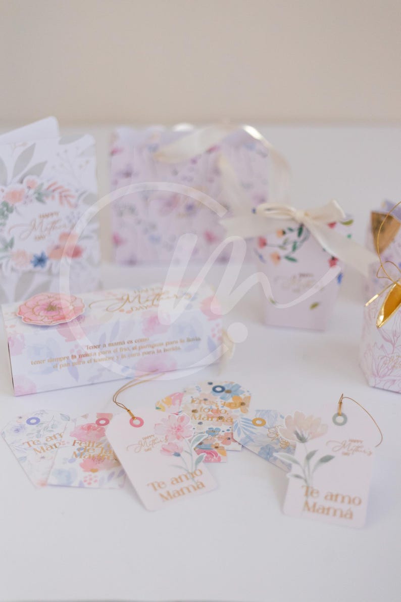 K&ouml;nnte beinhalten: Geschenkboxen und Anh&auml;nger mit floralen Designs. Die Boxen und Anh&auml;nger sind mit pastellfarbenen Blumen und den Texten "Happy Mother's Day" und "Te amo Mam&aacute;" verziert. Die Boxen sind mit B&auml;ndern gebunden.