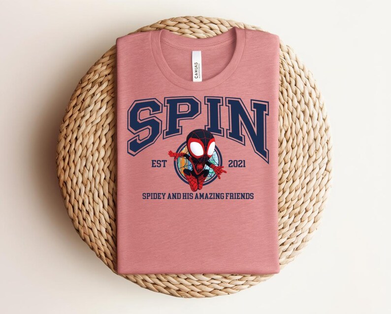K&ouml;nnte beinhalten: Staubrosafarbenes T-Shirt mit Rundhalsausschnitt, mit dem Wort "SPIN" in marineblauen Blockbuchstaben mit wei&szlig;er Umrandung. Darunter befindet sich ein Cartoon-Bild eines Superhelden. Der Text "EST 2021" und "SPIDEY AND HIS AMAZING FRIENDS" sind ebenfalls aufgedruckt.