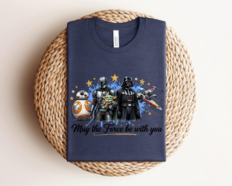 Pode incluir: Uma t-shirt azul-marinho de gola redonda com uma estampa gr&aacute;fica de BB-8, o Mandaloriano, Grogu e Darth Vader ao lado de um ca&ccedil;a estelar X-wing. O design inclui estrelas amarelas, salpicos de tinta azul e o texto May the Force be with you.
