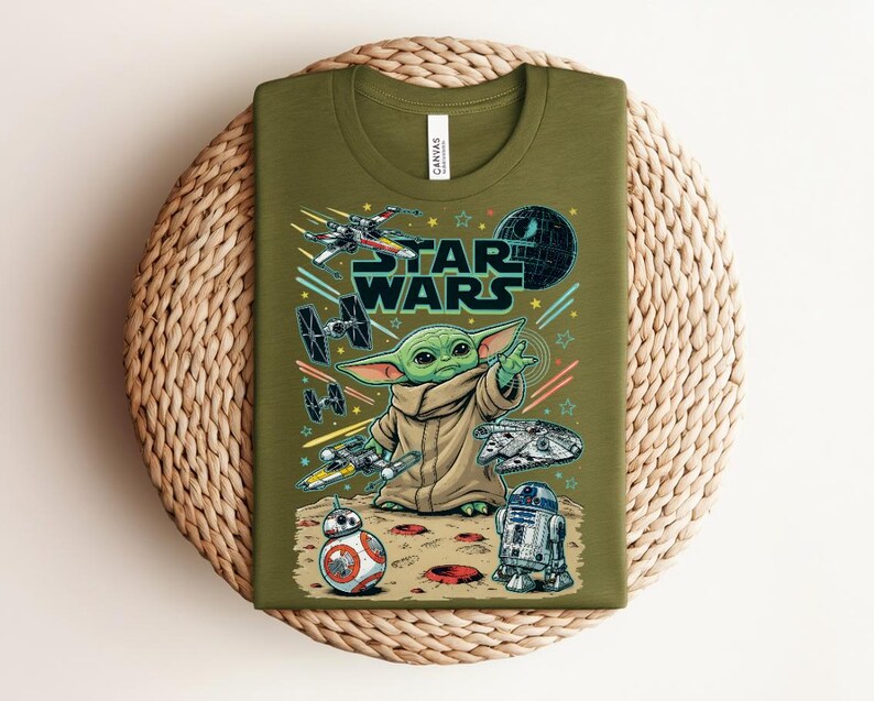 Puede incluir: Una camiseta de color verde oliva con un estampado gr&aacute;fico de Grogu de Star Wars, rodeado de varias naves espaciales, la Estrella de la Muerte, BB-8 y R2-D2. El texto STAR WARS aparece impreso en letras grandes sobre el personaje en el frente.