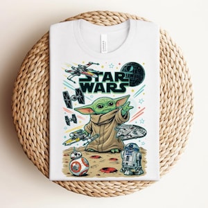 Puede incluir: Una camiseta blanca con un estampado gr&aacute;fico colorido de Star Wars. El dise&ntilde;o incluye un personaje verde con una t&uacute;nica beige, un X-wing, un caza TIE, el Halc&oacute;n Milenario, BB-8, R2-D2 y la Estrella de la Muerte sobre un fondo de estrellas y l&iacute;neas.