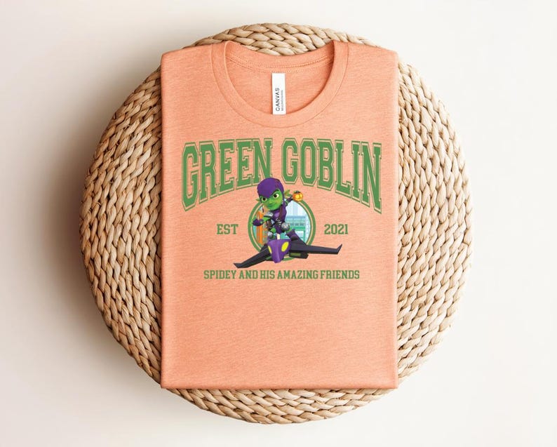 May include: Peach-colored t-shirt featuring the text "GREEN GOBLIN" in green lettering, with a cartoon illustration of the Green Goblin character. The shirt also includes the text "EST 2021" and "SPIDEY AND HIS AMAZING FRIENDS".
