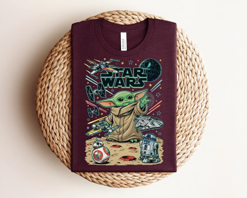 Puede incluir: Una camiseta de cuello redondo color granate con un estampado gr&aacute;fico de Star Wars. El dise&ntilde;o incluye a Grogu, BB-8, R2-D2, el Halc&oacute;n Milenario, un X-wing y un TIE fighter sobre un fondo espacial con el texto Star Wars en letras verdes.