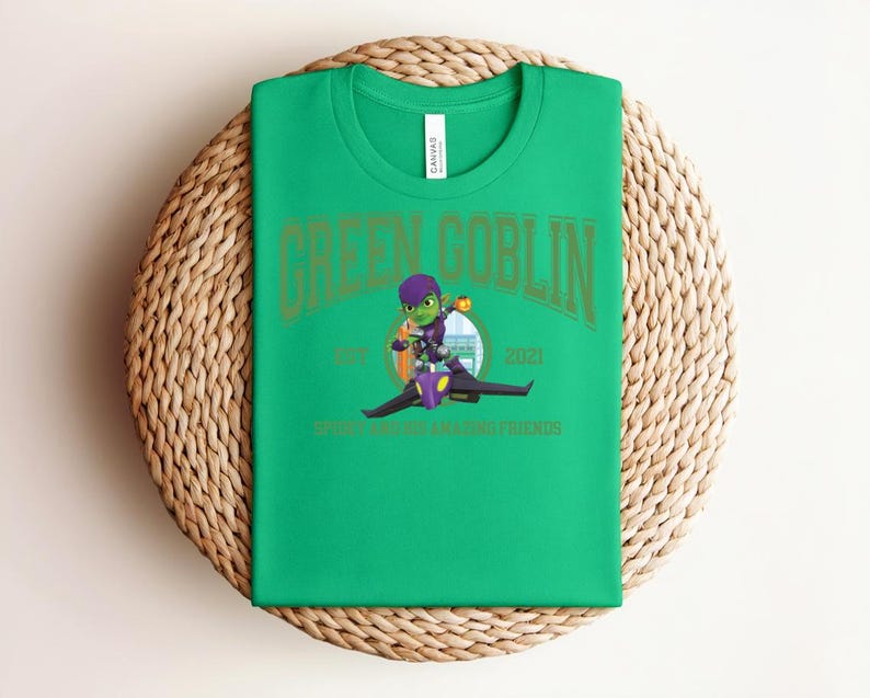 May include: A bright green t-shirt featuring the words "GREEN GOBLIN" in gold lettering. Below the text is a cartoon image of the Green Goblin riding a glider. The text "EST. 2021" and "SPIDER-MAN AND AMAZING FRIENDS" are also visible.