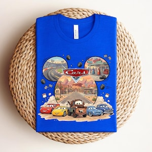 Puede incluir: Una camiseta azul real con un estampado gr&aacute;fico del logotipo de Disney Pixar Cars y personajes como Rayo McQueen, Mate y otros. El dise&ntilde;o est&aacute; dispuesto en forma de orejas de Mickey Mouse con escenas de una pista de carreras y Radiator Springs.