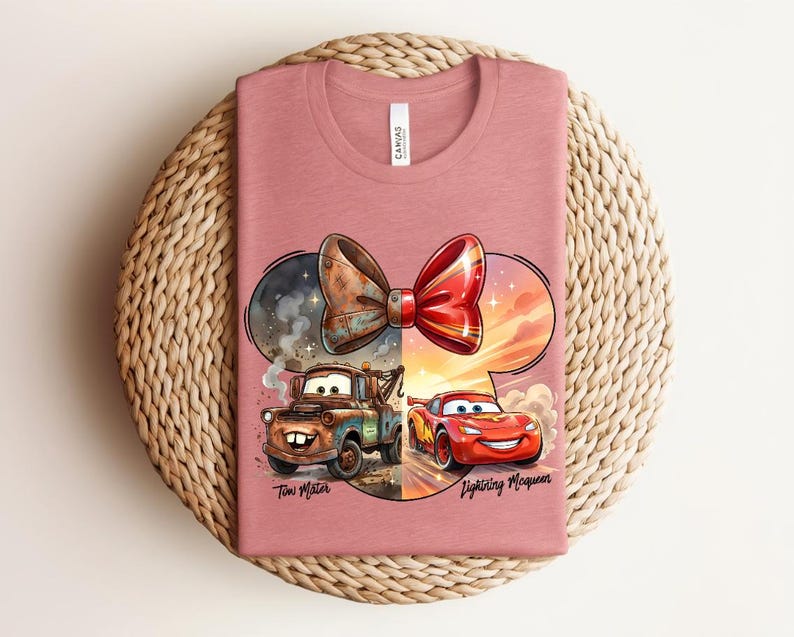 May include: A dusty rose crew neck t-shirt featuring a graphic of a mouse ear silhouette containing a rusty tow truck on the left and a red race car on the right, topped with a bow. The text reads Tow Mater and Lightning McQueen.