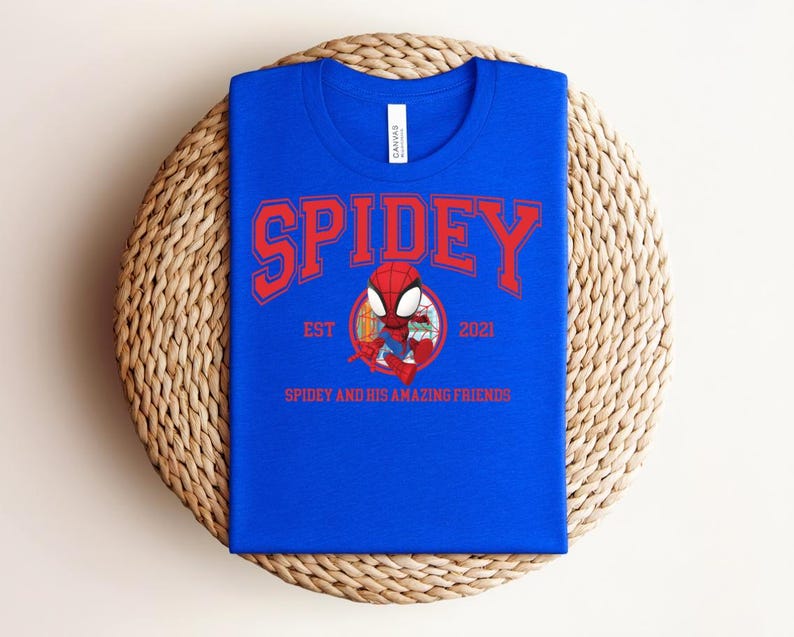 May include: A royal blue t-shirt with the word "SPIDEY" in red arched lettering. Below the word "SPIDEY" is a cartoon image of Spider-Man. The text "EST 2021" and "SPIDEY AND HIS AMAZING FRIENDS" are also printed on the shirt.
