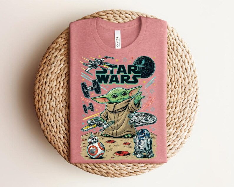 Puede incluir: Una camiseta de cuello redondo en color rosa empolvado con un estampado gr&aacute;fico de Star Wars. El dise&ntilde;o incluye a Grogu, BB-8, R2-D2, el Halc&oacute;n Milenario, un X-wing, cazas TIE y la Estrella de la Muerte. El texto STAR WARS aparece en may&uacute;sculas.