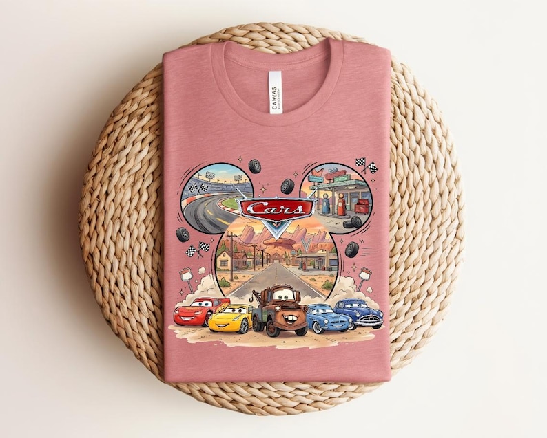 Puede incluir: Una camiseta de color rosa polvoriento con un gr&aacute;fico del logotipo y los personajes de Cars de Disney Pixar, incluyendo a Rayo McQueen y Mate. El dise&ntilde;o incluye un marco con forma de orejas de Mickey con escenas de una pista y Radiator Springs.