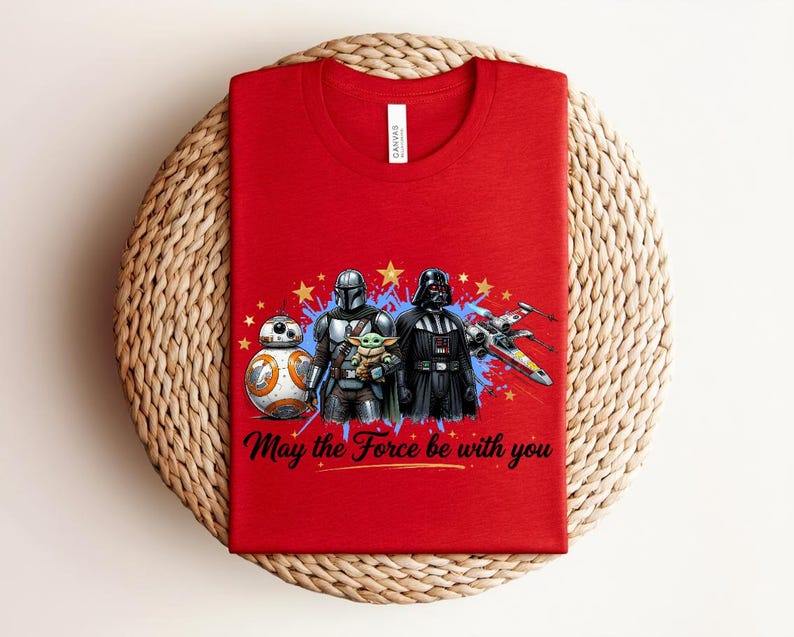 Pode incluir: Uma t-shirt vermelha com uma estampa gr&aacute;fica de BB-8, o Mandaloriano, Grogu e Darth Vader ao lado de um ca&ccedil;a estelar X-wing. O design inclui estrelas amarelas, salpicos de tinta azul e o texto May the Force be with you em preto.