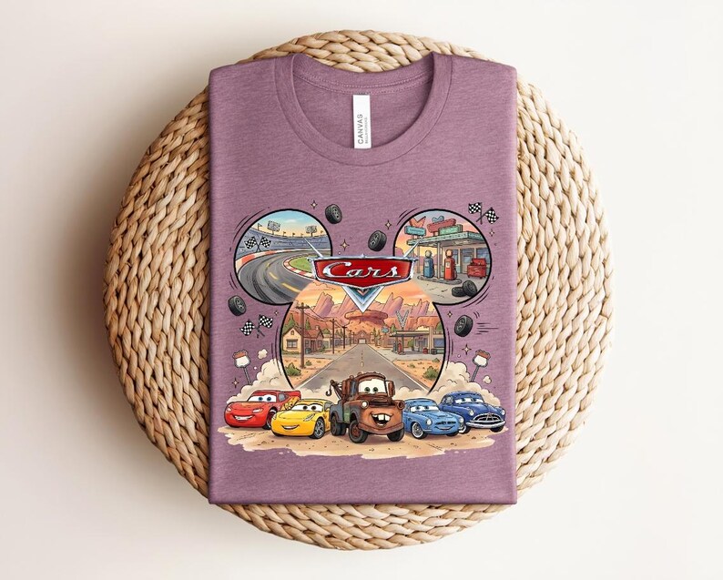 Puede incluir: Una camiseta malva de cuello redondo con un estampado gr&aacute;fico del logotipo de Disney Pixar Cars sobre tres escenas circulares de un circuito, una gasolinera y un pueblo del desierto. Debajo, cinco coches animados aparecen en la carretera.