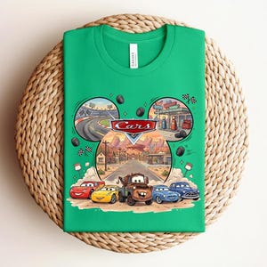 Puede incluir: Una camiseta de color verde brillante con un estampado gr&aacute;fico del logotipo de Disney Pixar Cars y personajes como Rayo McQueen, Mate y otros. El dise&ntilde;o incluye escenas circulares de una pista de carreras y una gasolinera sobre los personajes.