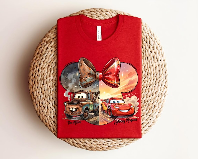 May include: A red t-shirt featuring a graphic of a bow shape containing two cars. On the left, a brown rusty tow truck labelled Tow Mater. On the right, a red race car labelled Lightning McQueen. The design includes smoke and sunset elements.