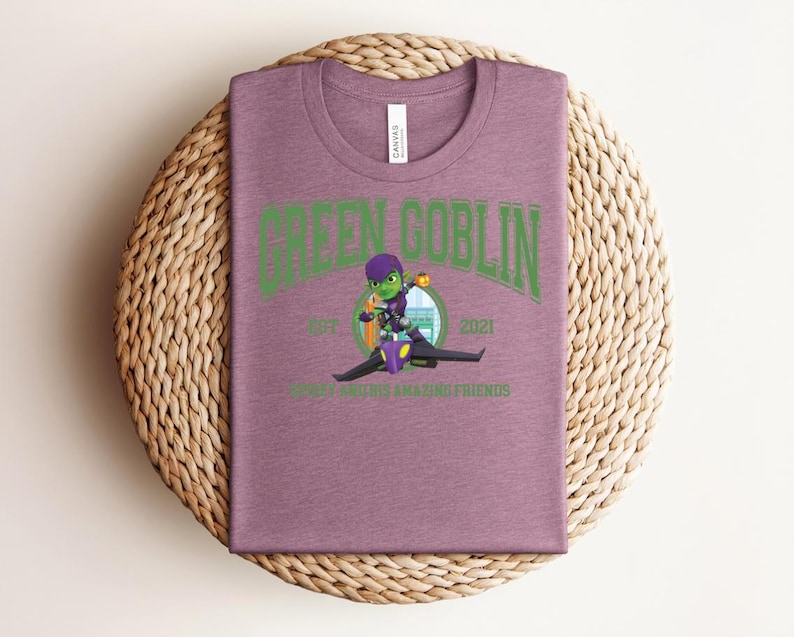 May include: A mauve t-shirt with a crew neck featuring a green graphic of the Green Goblin character riding a glider. The text "GREEN GOBLIN" arches across the top, with "EST 2021" and "ROGUE AND HIS AMAZING FRIENDS" below the image.