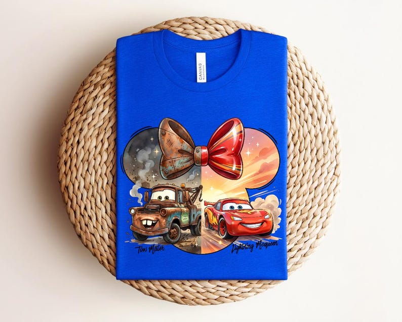 May include: A bright blue t-shirt featuring a graphic of Tow Mater and Lightning McQueen from the movie Cars. The design is shaped like a mouse ear silhouette with a large bow on top. The text Tow Mater and Lightning McQueen is printed below.