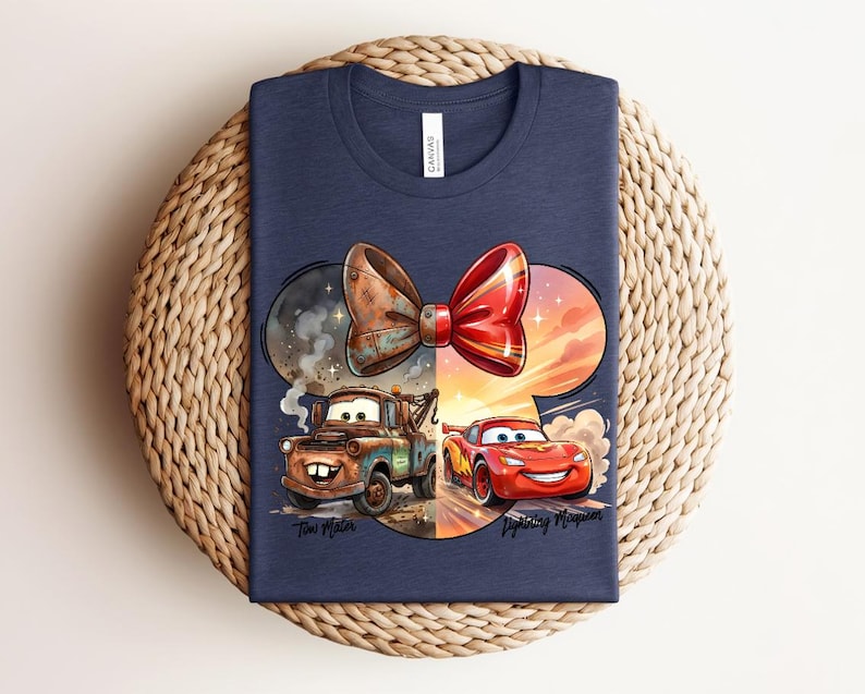 May include: A navy blue t-shirt featuring a graphic of a large bow shape containing two cartoon cars. On the left, a brown tow truck labelled Tow Mater is shown. On the right, a red race car labelled Lightning McQueen is depicted. The design is colourful.