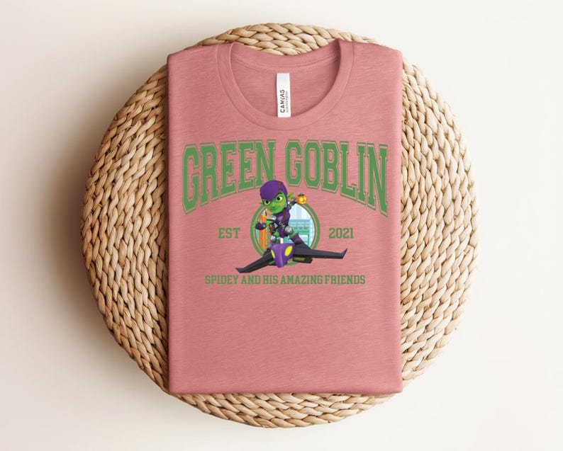 May include: A dusty rose t-shirt with a graphic of the Green Goblin riding a vehicle. The text "GREEN GOBLIN" arches across the top in green, with "EST 2021" below. The phrase "SPIDEY AND HIS AMAZING FRIENDS" is at the bottom.