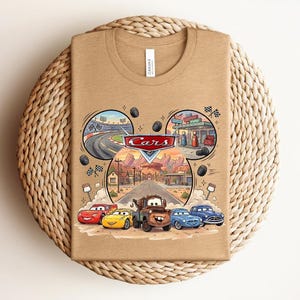 Puede incluir: Una camiseta de cuello redondo color canela con un estampado gr&aacute;fico de los personajes de Disney Pixar Cars, incluyendo a Rayo McQueen, Cruz Ram&iacute;rez, Mate y otros. El dise&ntilde;o incluye una escena de carretera, pista y logo.