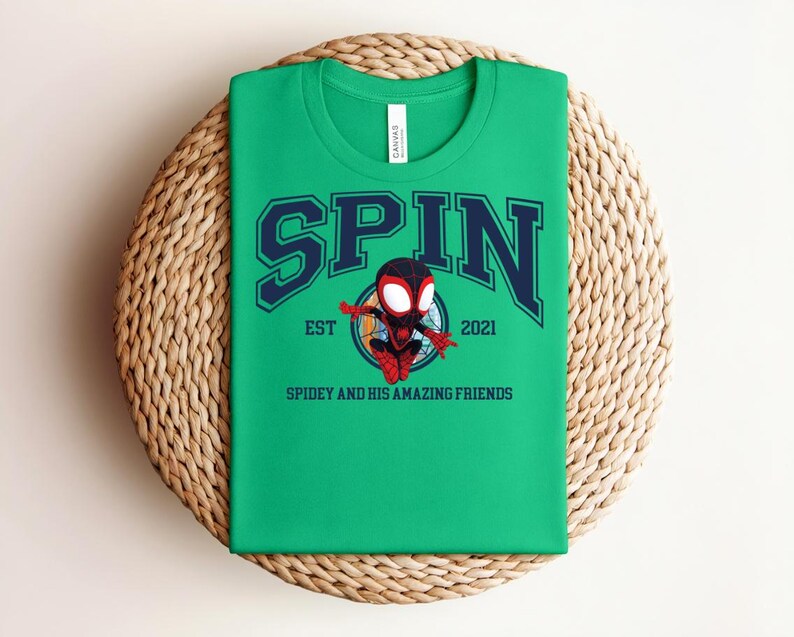 K&ouml;nnte beinhalten: Ein gr&uuml;nes T-Shirt mit dem Wort "SPIN" in marineblauen Blockbuchstaben mit wei&szlig;er Umrandung. Unter dem Wort "SPIN" befindet sich ein Cartoon-Bild eines Superhelden. Der Text "EST 2021" und "SPIDEY AND HIS AMAZING FRIENDS" sind ebenfalls auf dem T-Shirt aufgedruckt.