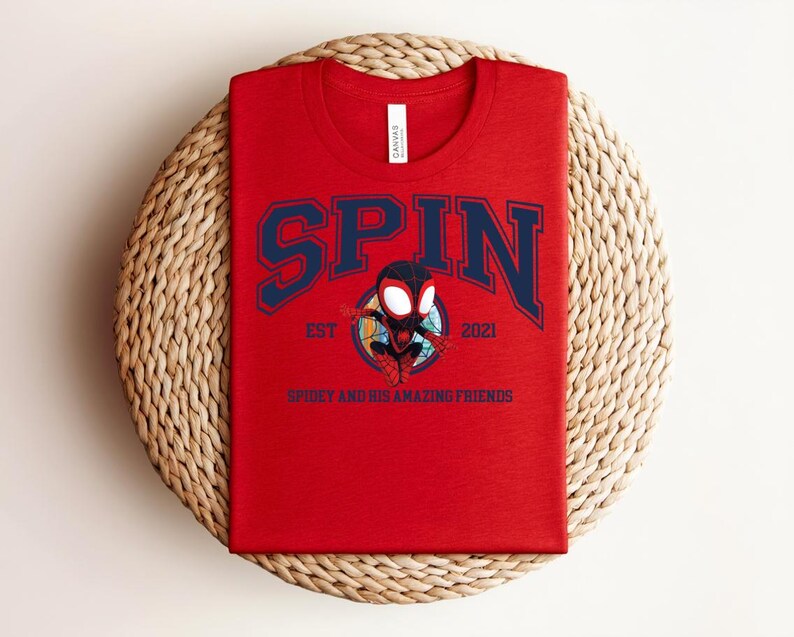 K&ouml;nnte beinhalten: Ein rotes T-Shirt mit dem Wort "SPIN" in marineblauen Blockbuchstaben. Unter dem Wort "SPIN" befindet sich ein Cartoon-Bild eines Superhelden. Der Text "EST 2021" und "SPIDEY AND HIS AMAZING FRIENDS" sind ebenfalls auf dem T-Shirt aufgedruckt.