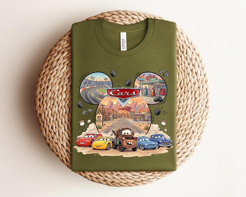 Puede incluir: Una camiseta verde oliva con un estampado gr&aacute;fico del logotipo de Disney Pixar Cars y personajes como Rayo McQueen, Mate y otros. El dise&ntilde;o incluye escenas circulares de una pista de carreras y una gasolinera sobre una carretera del desierto.