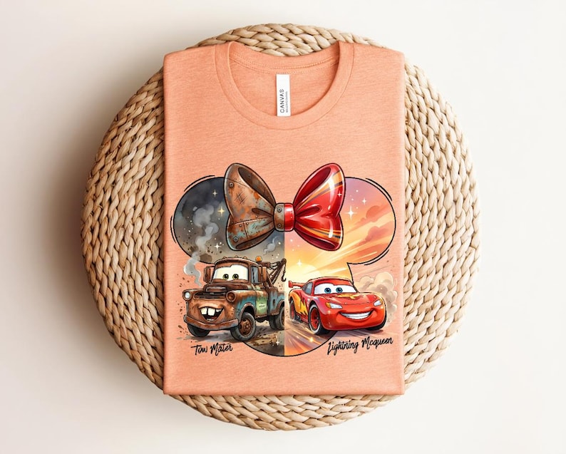 May include: A peach-coloured t-shirt featuring a graphic of a bow shape containing Tow Mater on the left and Lightning McQueen on the right. The text Tow Mater and Lightning McQueen is printed below the respective characters in a black script font.
