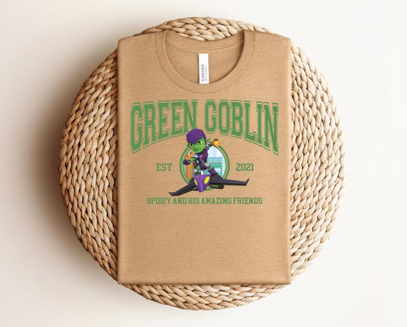 May include: A tan t-shirt featuring the text "GREEN GOBLIN" in green, with a cartoon image of the Green Goblin riding a glider. The text "EST 2021" and "SPIDEY AND HIS AMAZING FRIENDS" are also printed on the shirt.