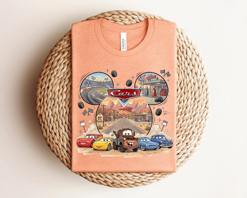 Puede incluir: Una camiseta color melocot&oacute;n con un gr&aacute;fico del logotipo de Disney Pixar Cars y personajes como Rayo McQueen, Mate y otros. El dise&ntilde;o est&aacute; dispuesto en forma de orejas de Mickey Mouse con escenas de una pista de carreras y Radiator Springs.