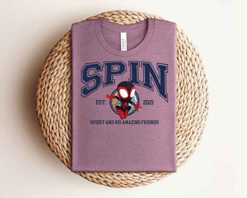 K&ouml;nnte beinhalten: Ein mauvefarbenes T-Shirt mit dem Wort "SPIN" in marineblauen Buchstaben. Darunter befindet sich ein Cartoon-Bild von Spidey, mit dem Text "EST 2021" und "SPIDEY AND HIS AMAZING FRIENDS".